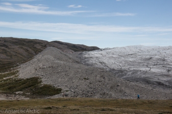 A man in blue stands for scale in front of the glacial edge and a moraine